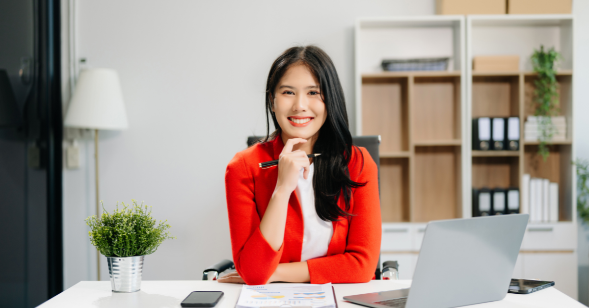 what is a virtual assistant, smiling virtual assistant working at a desk with a laptop and reports in an office